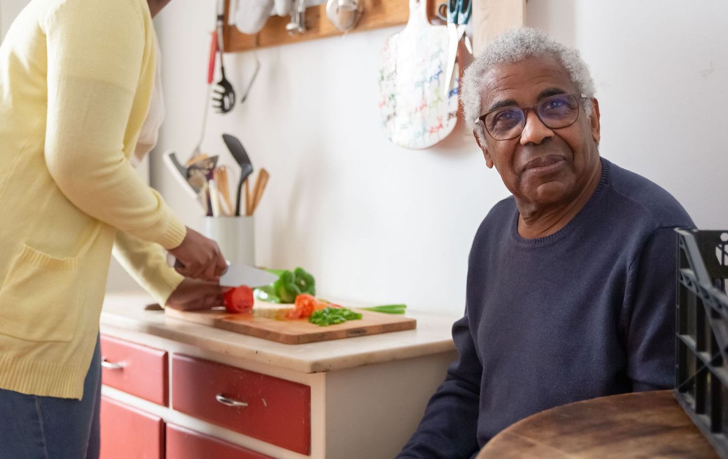 Elderly man and adult woman cooking together in a cozy kitchen setting.